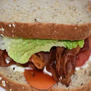 A forward facing shot of a BLT sandwich on untoasted brown bread, as plain as can be with the minimal number of ingredients