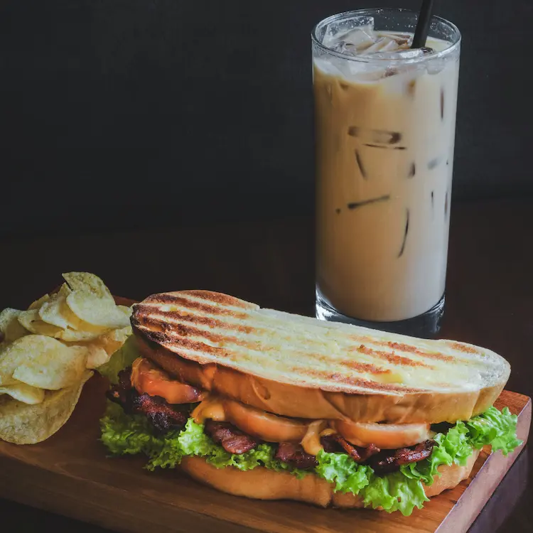 A grilled sandwich on sourdough bread sitting next to a side of chips and a creamy iced coffee. Ready for lunch.